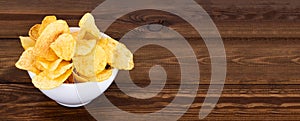 Crispy potato chips in bowl on wooden background, with copyspace