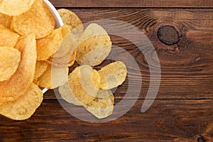 Crispy potato chips in bowl on wooden background, top view