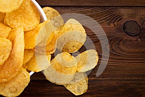 Crispy potato chips in bowl on wooden background, top view