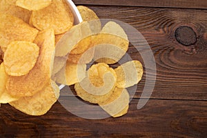 Crispy potato chips in bowl on wooden background, top view