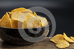 Crispy potato chips in a bowl on wooden with black background