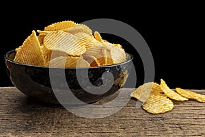 Crispy potato chips in a bowl on wooden with black background