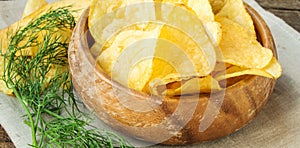 Crispy potato chips with dill in a wooden bowl on linen napkin