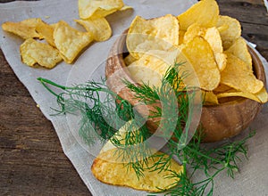 Crispy potato chips with dill in a wooden bowl on linen napkin