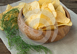Crispy potato chips with dill in a wooden bowl on linen napkin