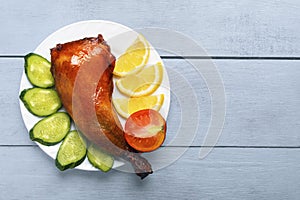 Crispy poultry meat, cooked on a grill with sliced lemon, cucumber and tomatoes on white plate on a wooden table background. Copy