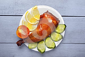 Crispy poultry meat, cooked on a grill with sliced lemon, cucumber and tomatoes on white plate on a wooden table background. Natur