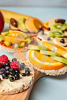 Crispy puffed rice cakes on table with fresh fruit kiwi banana apple blueberries raspberries and orange on the table - close up