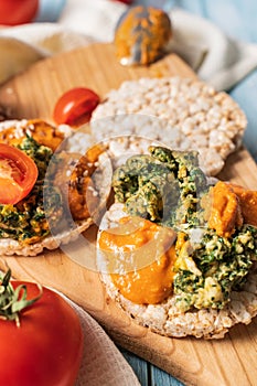 Crispy puffed rice cakes on table with hummus spread spinach with eggs and tomato and vegetables on the table - close up view on