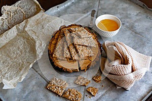 Crispy rectangular crispbreads with sesame seeds and seeds with natural honey in an interestingly decorated composition with wood