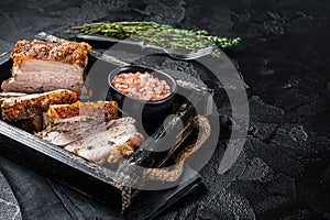 Crispy Roast Pork Belly. Sliced roasted meat with crust in a tray with spices. Black background. Top view. Copy space