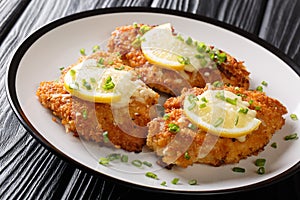 Crispy romano chicken breast fried breaded served with lemon and green onion close-up on a plate. horizontal