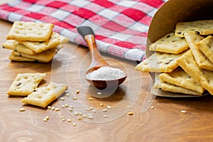 Crispy salted crackers, wooden spoon with salt crystalls, paper bag full of crackers on a red napkin on wooden table. photo