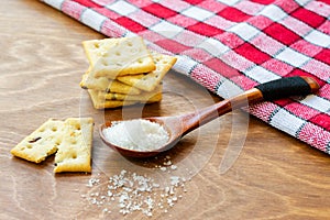Crispy salted crackers, wooden spoon with salt crystalls, paper bag full of crackers on a red napkin on wooden table. photo