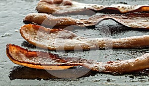 Crispy strips of bacon frying on a cast iron griddle pan.