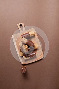 Crispy wafer rolls half-coated in milk chocolate on wooden serving board on brown background. Top view, copy space