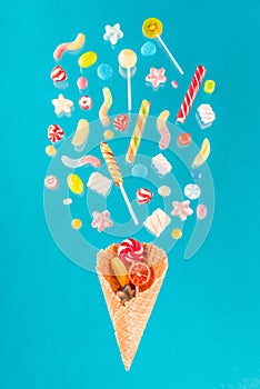 Crispy waffle cone with sweet candies and lollipops on blue