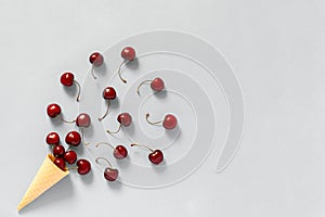 Crispy waffle ice cream cone with scattered red ripe sweet cherries. Still life on grey background. Copy space, Flat lay, Top view