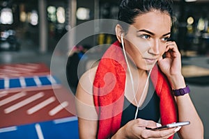 Crlose up portrait of a beautiful smiling and sporty young woman listening to music from her smartphone, having a break after