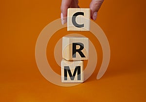 CRM - Customer relationship management symbol. Concept word CRM on wooden cubes. Businessman hand. Beautiful orange background.