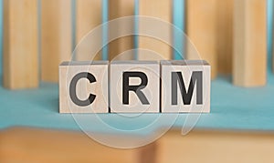 CRM Customer Relationship Marketing written on a wooden cubeon a blue table with wooden background.. Business concept