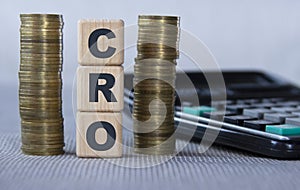 CRO - acronym on wooden cubes on the background of coins and calculator