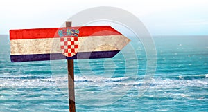 Croatia flag on wooden table sign on beach background. There is beach and clear water of sea and blue sky