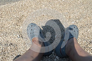 Croatian pebble beach with legs and reflection of man with hat.