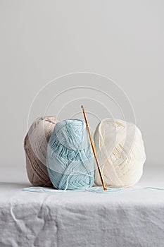 Crochet hook and balls of cotton yarn pastel colors on a white table