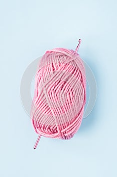 Crochet hook with balls of pink yarn on a blue background
