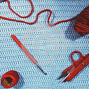 Crochet hook, scissors, yarn and woolen ball on crocheted cloth