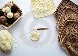 Crochet on a white background. Balls of brown yarn, crochet hook, square motifs. flat lay