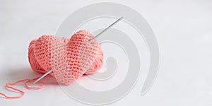 Crocheted amigurumi pink heart with crochet hook and skein of yarn on a white background. Valentine's day banner