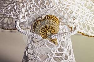 Crocheted golden heart in the hands of a white angel knotted by crotchet. Concept of love and amulet