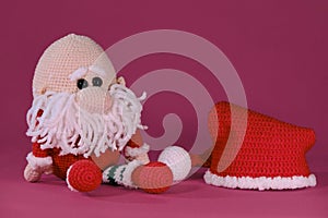 Crocheted santa claus, handmade art. Amigurumi one bald Christmas gnome with red hat and white beard sits on pink