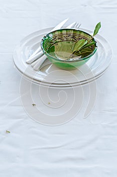 Crockery and cutlery with some bay leaves inside a green bowl.