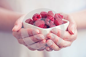 Crockery with raspberries in woman hands