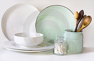 Crockery, tableware, utensils and other different white and turquoise stuff on white table-top. Kitchen still life as background f