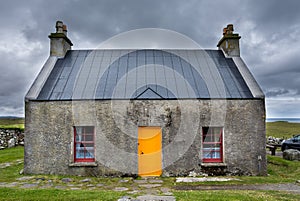 The croft house whitehouse, with orange door and dark red windows, on a stormy, cloudy day