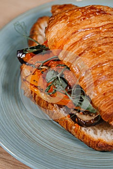 Croissant with baked vegetables lies on a plate on the table close-up