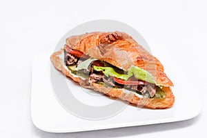 Croissant with beef, pickled cucumber, tomato and lettuce on a white background.