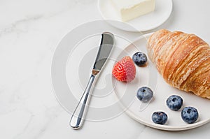 Croissant with berries in white bowl and oil knife on white stone background. Copy space