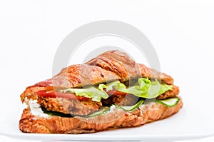 Croissant with chicken cutlet, fresh cucumber, tomato and lettuce on a white background.