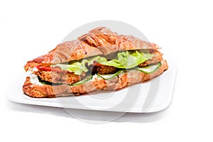 Croissant with chicken cutlet, fresh cucumber, tomato and lettuce on a white background.