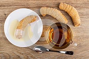 Croissant with condensed milk on saucer, croissants, cup of tea, spoon on table. Top view