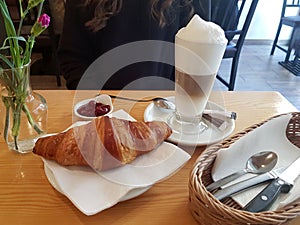 Croissant and a fresh coffee alongside with flowers and tableware on an elegant table