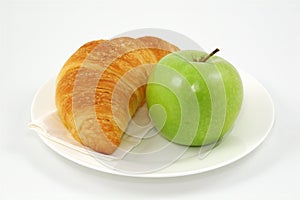 Croissant and green apple on plate