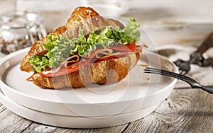 Croissant with ham, cheese, tomato and fresh salad on a white plate. Morning food still life. Tasty breakfast