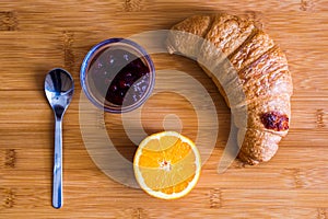 Croissant, jam and orange slice on wooden table