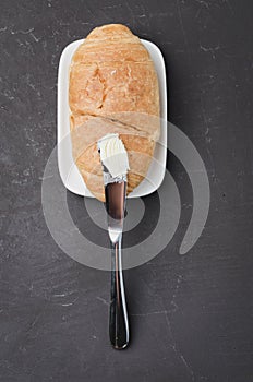 Croissant and a knife with butter on a dark stone background. Top view. French breakfast